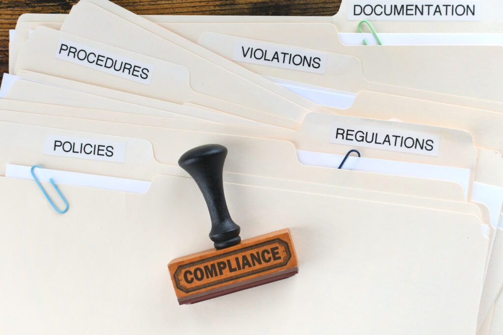 Compliance rubber stamp on folders marked Policies Regulations Violations Procedures Documentation.