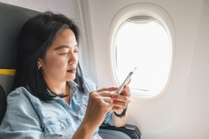 Asian Woman sitting at window seat in airplane and turn on airplane mode on mobile